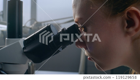 In medical laboratory, female microbiologist looks under microscope 119129658