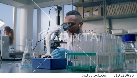 African American male microbiologist in white coat examines new sample of virus 119129659