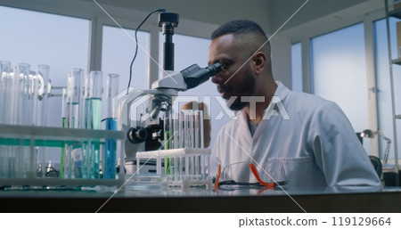African American male microbiologist in white coat examines new sample of virus African American male microbiologist in white coat examines new sample of virus 119129664