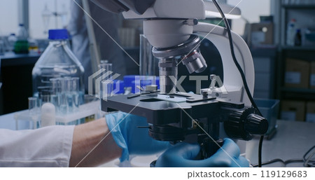 Close up of professional scientist putting slide with test sample under microscope 119129683