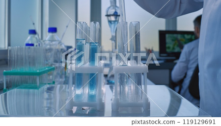 Professional scientist pours liquid from glass flask in test tubes for analysis with pipette 119129691