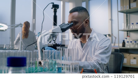 Bright medical science lab: African American microbiologist looks under microscope Bright medical science lab: African American microbiologist looks under microscope 119129701