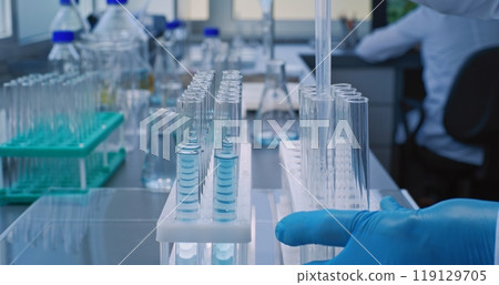 Close up of chemist taking liquid with pipette from glass flask, pouring into test tubes 119129705