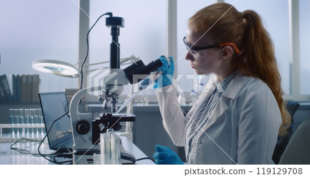 Female microbiologist looks under microscope, does analysis of test sample 119129708