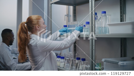 Female chemist takes test tubes from shelf with lab glassware 119129727