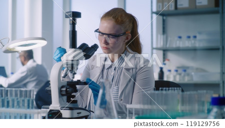Female biochemist takes liquid from test tube, looks under microscope Female biochemist takes liquid from test tube, looks under microscope 119129756