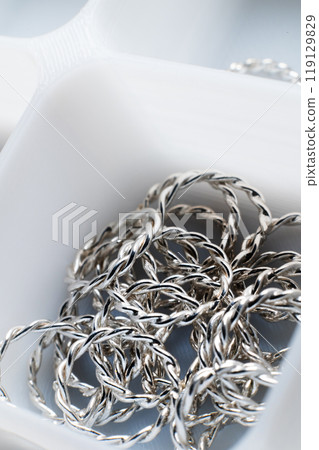 Close-up macro shot of small silver jewelry pieces lying in a white mesh box. DIY jewelry 119129829