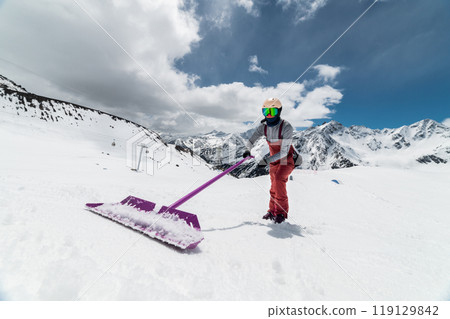 Snowboarder building a ski jump outdoors near a ski resort in the mountains, shaping a snowboard park. Sunny winter day 119129842