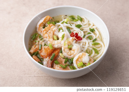 Asian dish with broth, noodles, tiger shrimp, fish and green onions. Traditional Asian soup in a white deep plate. Selective focus, close-up. Asian dish with broth, noodles, tiger shrimp, fish and green onions. Traditional Asian soup in a white deep plate. Selective focus, close-up. 119129851