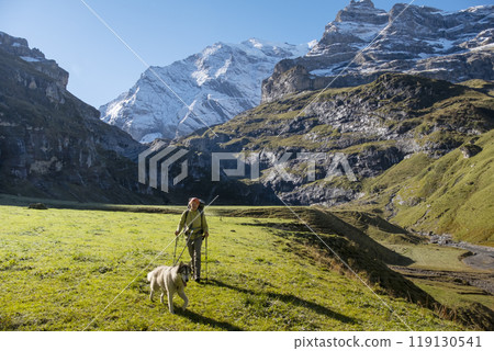 Woman with dog in Switzerland mountain valley Kiental, Berner Oberland Alps. Snow mountains, sunny weather, travel to Swiss, travelling with pet. 119130541