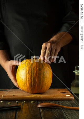 Chef prepares a large ripe pumpkin with spices on the kitchen table. Low-key concept of a fruit diet or cooking a national dish with pumpkin Chef prepares a large ripe pumpkin with spices on the kitchen table. Low-key concept of a fruit diet or cooking a national dish with pumpkin 119131625