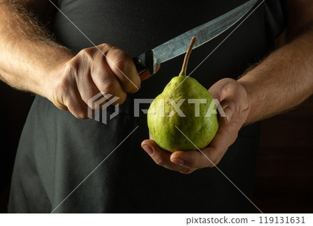 Knife and green large pear in hands of cook before preparing fruit food for dietary breakfast. Cutting pears before eating 119131631