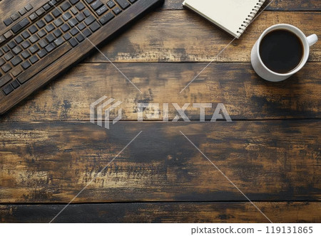 A wooden desk setup featuring a keyboard, cup of coffee, and a notepad in a cozy workspace 119131865