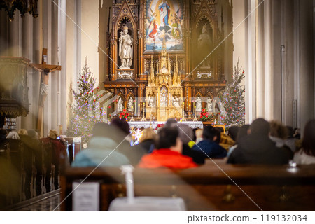 Church altar during Christmas Mass with The Nativity scene. Back view of sitting parishioners. The Catholic Orthodox Christmas holiday in Europe Church altar during Christmas Mass with The Nativity scene. Back view of sitting parishioners. The Catholic Orthodox Christmas holiday in Europe 119132034