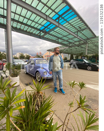 Man standing in front of vintage violet car on the street in summer. Old-fashioned nostalgia and retro style concept 119132186