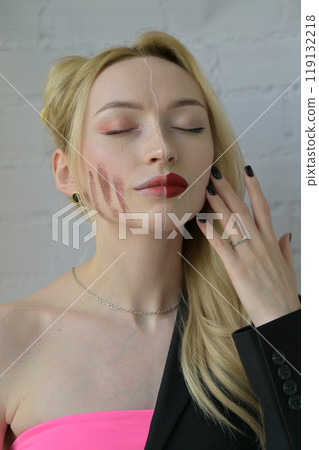 Close-up portrait of a blonde girl with different make-up on half of her face with hand near face on white background Close-up portrait of a blonde girl with different make-up on half of her face with hand near face on white background 119132218