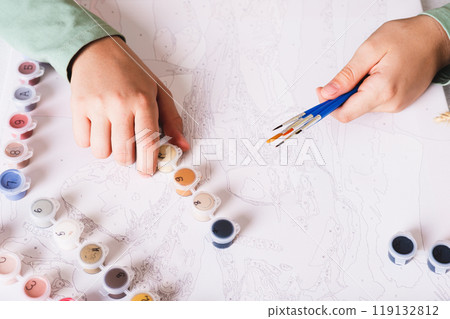 Girl's hands holding brushes and paints for painting by numbers Girl's hands holding brushes and paints for painting by numbers 119132812