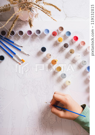 A girl paints a picture by numbers with a brush using a paint set top and vertical view 119132815