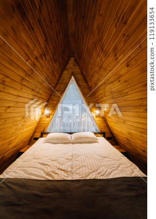 Cozy wooden cabin bedroom with large bed and natural light, creating a warm and inviting atmosphere 119133654