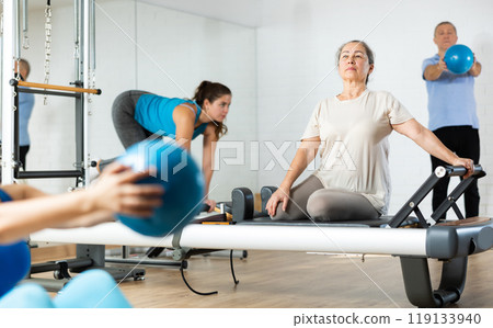 Senior woman doing stretching exercises on pilates reformer Senior woman doing stretching exercises on pilates reformer 119133940