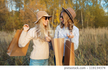 Fashionable happy young two women friends with shopping bags, stylish smiling girlfriends in park 119134374