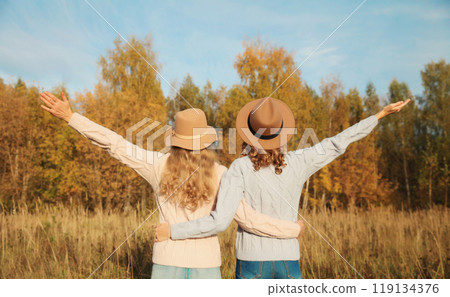 Back view, happy two women friends enjoying in autumn park, stylish girlfriends together outdoors 119134376
