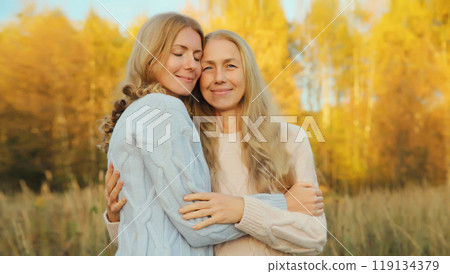 Happy two women, smiling mature mother and adult daughter hugging in autumn park 119134379