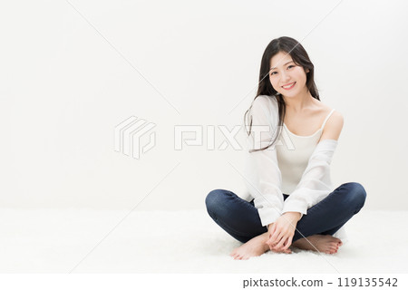 A young woman sitting cross-legged in skinny jeans, denim pants 119135542