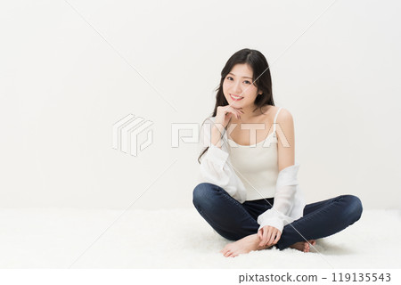 一位年輕女子穿著緊身牛仔褲、牛仔褲和牛仔褲,盤腿而坐 一位年輕女子穿著緊身牛仔褲、牛仔褲和牛仔褲,盤腿而坐 119135543