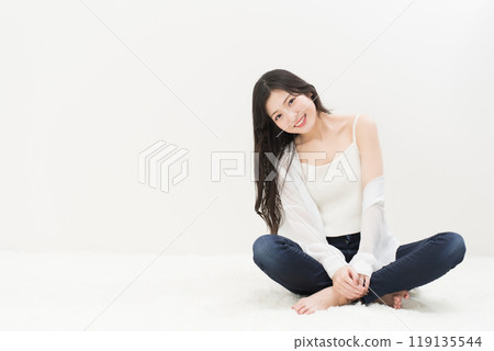 一位年輕女子穿著緊身牛仔褲、牛仔褲和牛仔褲,盤腿而坐 一位年輕女子穿著緊身牛仔褲、牛仔褲和牛仔褲,盤腿而坐 119135544