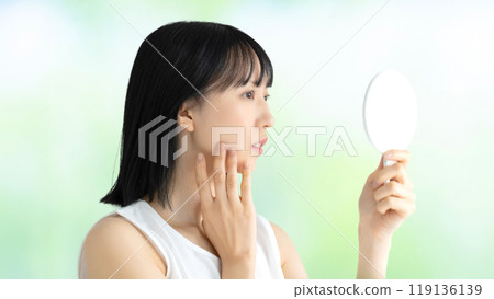 一位年輕女子在鏡子裡檢視自己皮膚的美麗形象 一位年輕女子在鏡子裡檢視自己皮膚的美麗形象 119136139