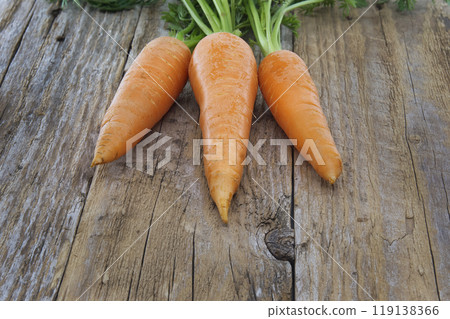 Bunch of bright orange carrots with lush green tops on rustic table 119138366