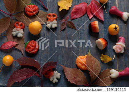 Frame of fall leaves, candy for Halloween. Holidays and food. Dessert in the shape of a pumpkin, skull, witch. Background for design.  119139515