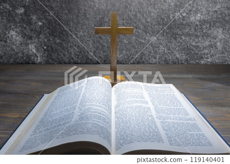 Wooden religion cross and opened blue book of Holy Bible. It is laying on a wooden table. Religious christian holiday. Symbol of faith in God, Christianity Feast Wooden religion cross and opened blue book of Holy Bible. It is laying on a wooden table. Religious christian holiday. Symbol of faith in God, Christianity Feast 119140401