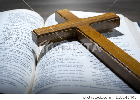 Wooden religion cross and opened blue book of Holy Bible. It is laying on a wooden table. Religious christian holiday. Symbol of faith in God, Christianity Feast Wooden religion cross and opened blue book of Holy Bible. It is laying on a wooden table. Religious christian holiday. Symbol of faith in God, Christianity Feast 119140403