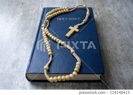 Wooden religion cross on rosary beads and blue book with the word Holy Bible. It is laying on a wooden table. Religious christian holiday. Symbol of faith in God, Christianity Feast Wooden religion cross on rosary beads and blue book with the word Holy Bible. It is laying on a wooden table. Religious christian holiday. Symbol of faith in God, Christianity Feast 119140415