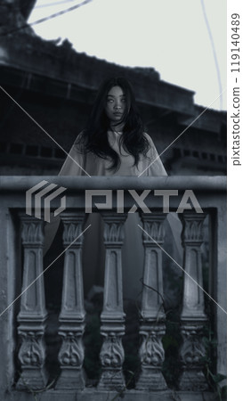 Woman ghost standing behind balustrade. Woman had long hair. The sky is dark and cloudy, and there is a abandoned building in the background. Scene is scary and creepy 119140489
