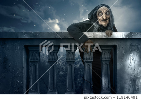 Old witch rising out behind balustrade with moonlight background. Scene is scary and creepy 119140491