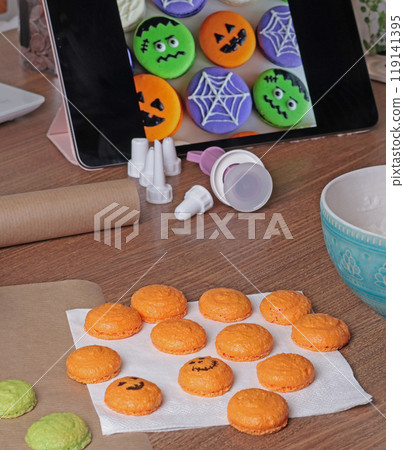 Halloween macarons. Pumpkins and monsters draw with food marker in kitchen. Baking macarons at home in close-up. Halloween macarons. Pumpkins and monsters draw with food marker in kitchen. Baking macarons at home in close-up. 119141395