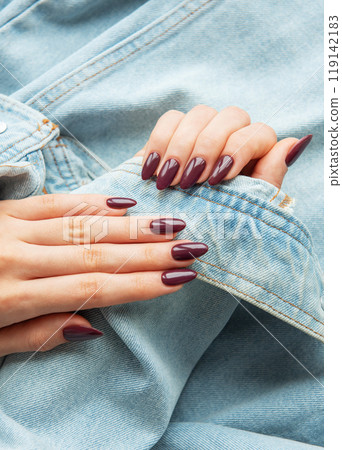 Elegant hands with polished burgundy nails resting on a denim jacket sleeve  119142183