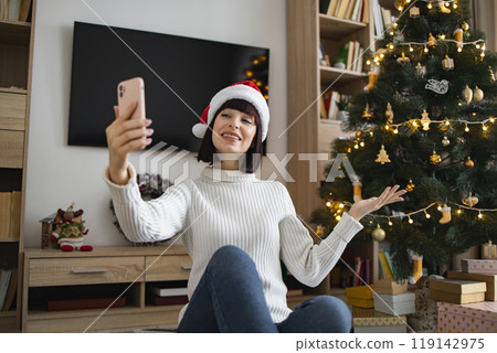Young woman enjoys video call by Christmas tree at home Young woman enjoys video call by Christmas tree at home 119142975