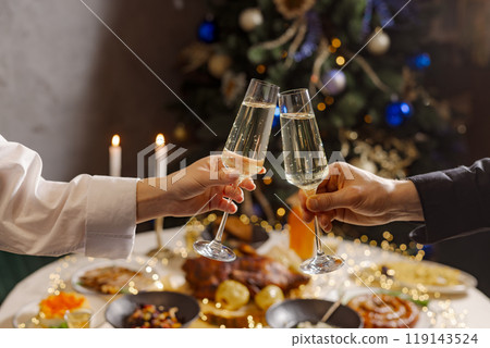 hands with glasses of champagne close-up on the background of a festive Christmas table 119143524