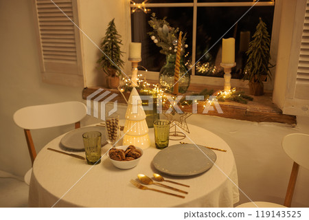 Cozy Christmas setting with a round table near the window, with a Christmas tree in the center Cozy Christmas setting with a round table near the window, with a Christmas tree in the center 119143525