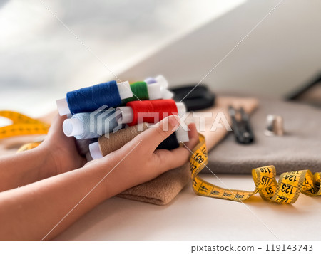 Childs hands holding colorful threads with sewing supplies on a creative workspace 119143743