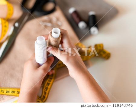 Hands holding thread spools for sewing with tape measure and fabric 119143746