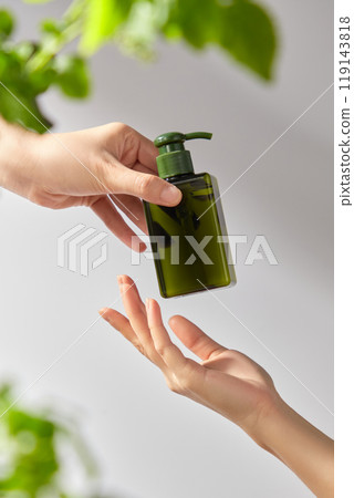 The image template for advertisement product nature features a hand gently holding a green bottle with a pump dispenser mockup against a soft white background with some green leaves. The image template for advertisement product nature features a hand gently holding a green bottle with a pump dispenser mockup against a soft white background with some green leaves. 119143818