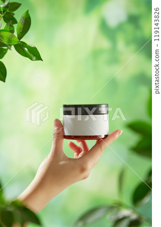 Ideal for a template ad promoting beauty care products, the image features a small brown glass jar with a black lid, centered in the model's hand against an outdoor backdrop, surrounded by greenery. Ideal for a template ad promoting beauty care products, the image features a small brown glass jar with a black lid, centered in the model's hand against an outdoor backdrop, surrounded by greenery. 119143826