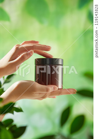 To demonstrate a sense of organic beauty, a mockup of a brown jar is carefully held by two hands against a background of vibrant green foliage. A sample for an advertising for a beauty care product. To demonstrate a sense of organic beauty, a mockup of a brown jar is carefully held by two hands against a background of vibrant green foliage. A sample for an advertising for a beauty care product. 119143828