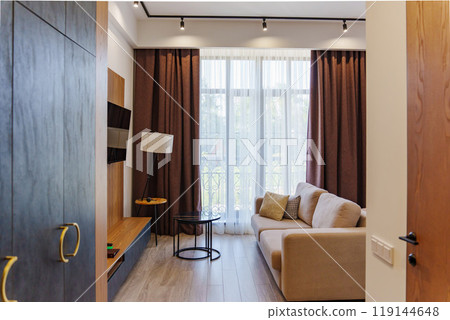 A cozy living room with large windows covered by brown curtains. A cozy living room with large windows covered by brown curtains. 119144648