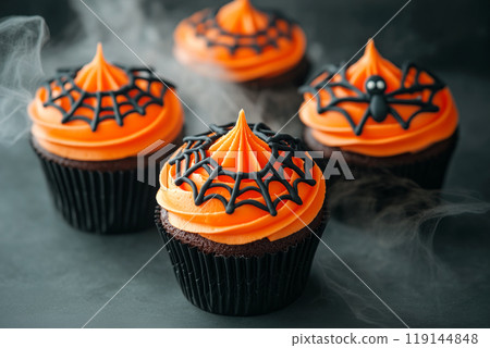 Chocolate cupcakes with orange frosting and black spider web decorations on light background. Halloween dessert concept 119144848